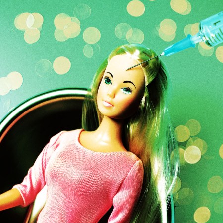 A Barbie doll sits in a chair with a needle near her head, suggesting a Botox injection