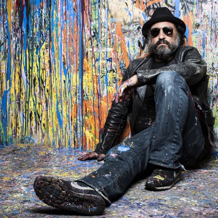 French street artist Mr. Brainwash poses in front of a wall splattered with spray paint