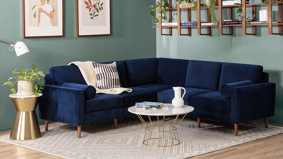 A blue performance velvet Nomad couch from Burrow. The modular sofa is pictured here in a living room next to a coffee table.