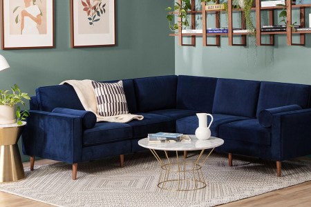 A blue performance velvet Nomad couch from Burrow. The modular sofa is pictured here in a living room next to a coffee table.
