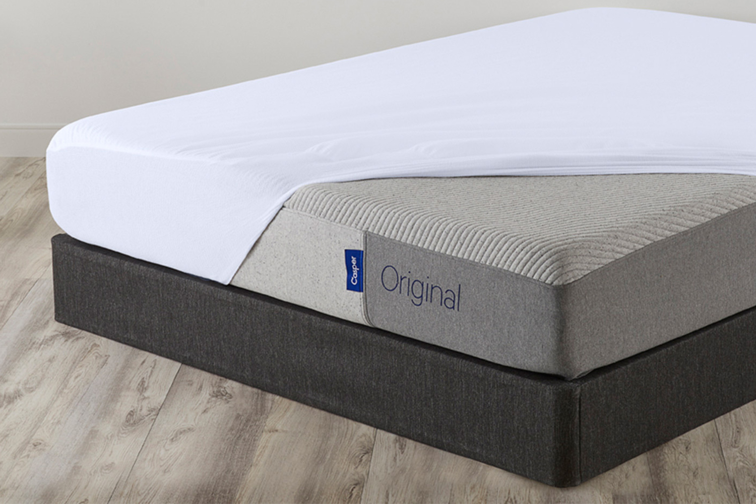 A Casper Original mattress with a mattress protector half on and sitting on a grey foundation. This bundle is on sale for Cyber Week 2021.