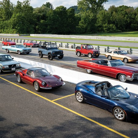 A race track with collector cars lined up, including the Tesla Roadster Sport, Ferrari 246 Dino, Land Rover Defender and others. They're all on the Hagerty Bull Market List for 2022.