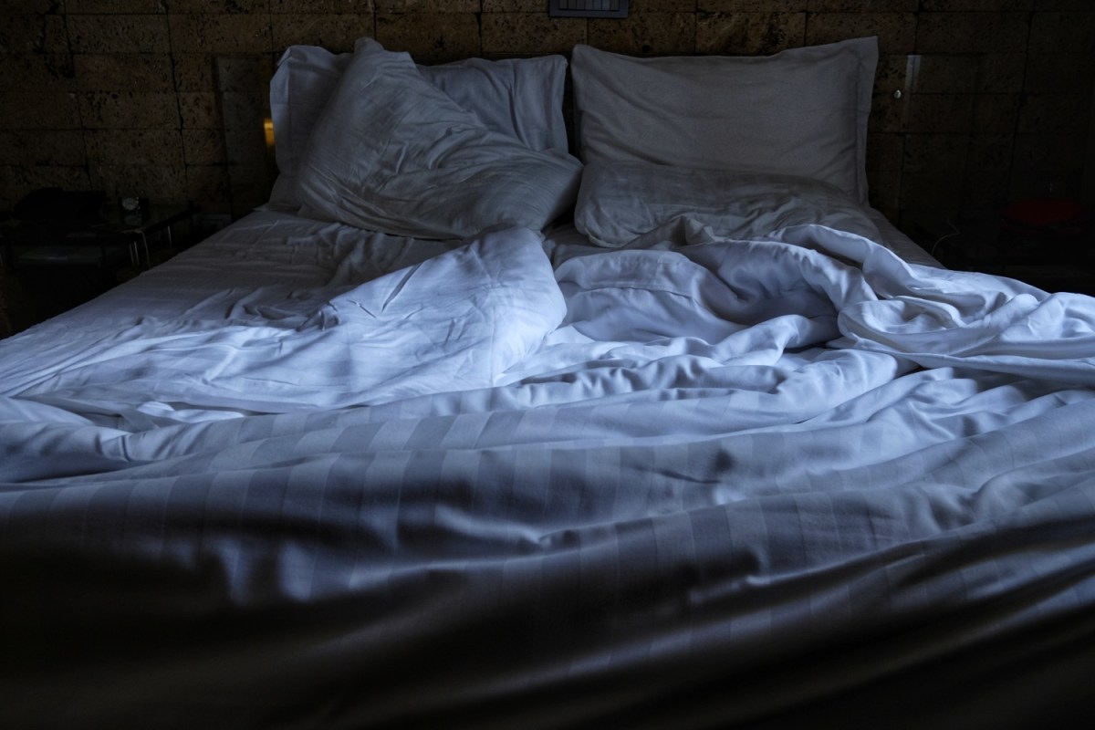 Rumpled sheets on an empty bed in a dark room