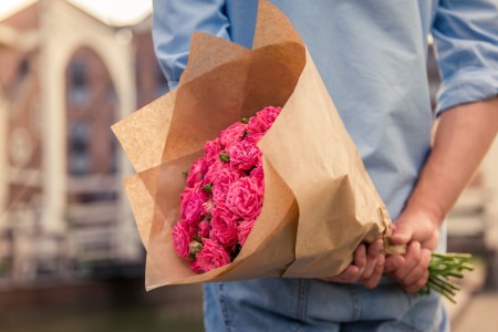 Man is holding flowers behind his back and waiting for his girlfriend, cropped
