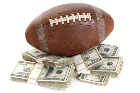 A football sits atop stacks of cash with money wrappers. A New Jersey man recently turned a $25 sports bet at Caesars Sportsbook into over $200,000.