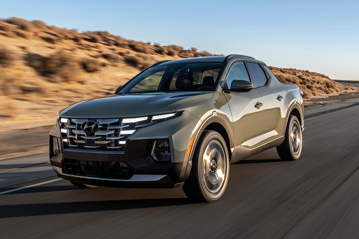 A 2022 Hyundai Santa Cruz in grey driving down the road. We reviewed the the small pickup truck to see how it compares to the midsize segment.