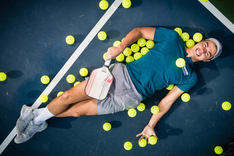 Ben Johns, the no. 1-ranked men's pickleball player in the world, lies on a pickleball court, surrounded by pickleballs