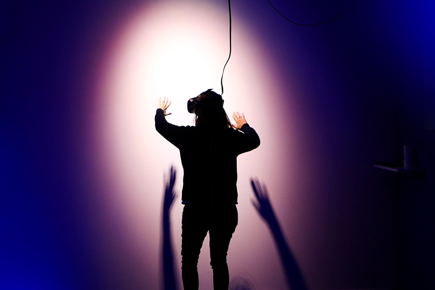 A person wearing a virtual reality headset facing a wall with a light shining down on them. VR games that are part of the metaverse are already experiencing problems of harassment.