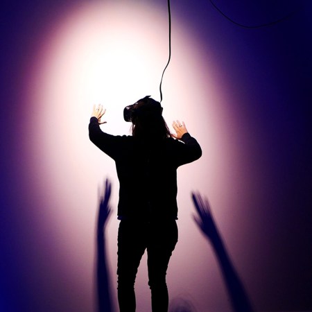 A person wearing a virtual reality headset facing a wall with a light shining down on them. VR games that are part of the metaverse are already experiencing problems of harassment.