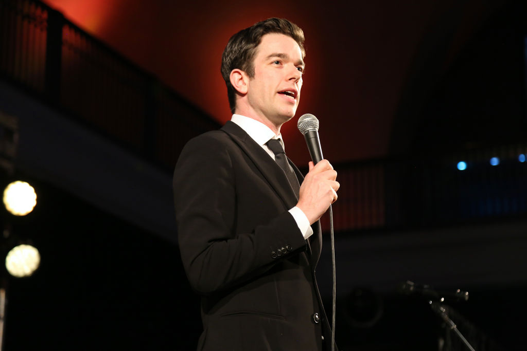 Comedian John Mulaney wearing a suit and tie and holding a microphone at the American Museum of Natural History's 2019 gala