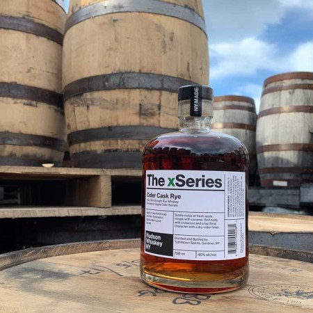 A bottle of Cider Cask Rye from Hudson Whiskey on top of barrels. The release is part of a new trend for whiskey brands to release ryes that have undergone secondary maturations