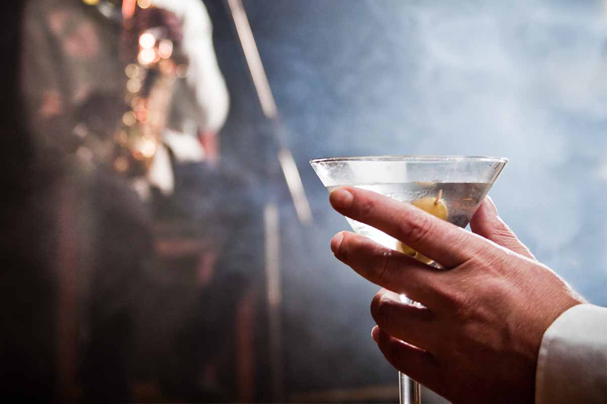 A man holding a martini in a smoky jazz nightclub. The Smoky Martini is an actual drink, though it usually doesn't contain olives.