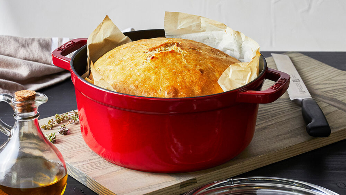 A red cocotte from Staub with a loaf of bread inside. The four-quart Dutch oven with a glass lid is on sale at Sur La Table for December 2021.