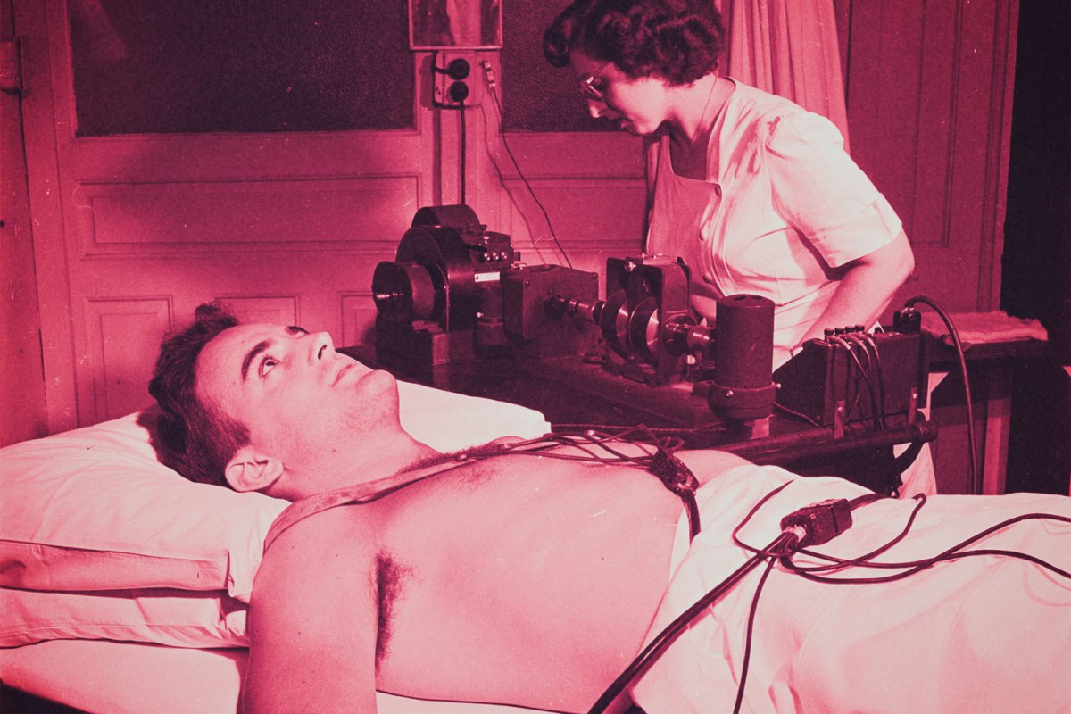 A man hooked up to a old-fashiond cardiograph machine.