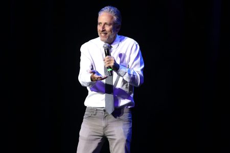 Jon Stewart in a white shirt and tie speaking into a microphone at the 10th Annual Stand Up For Heroes - Show at The Theater at Madison Square Garden on November 1, 2016 in New York City