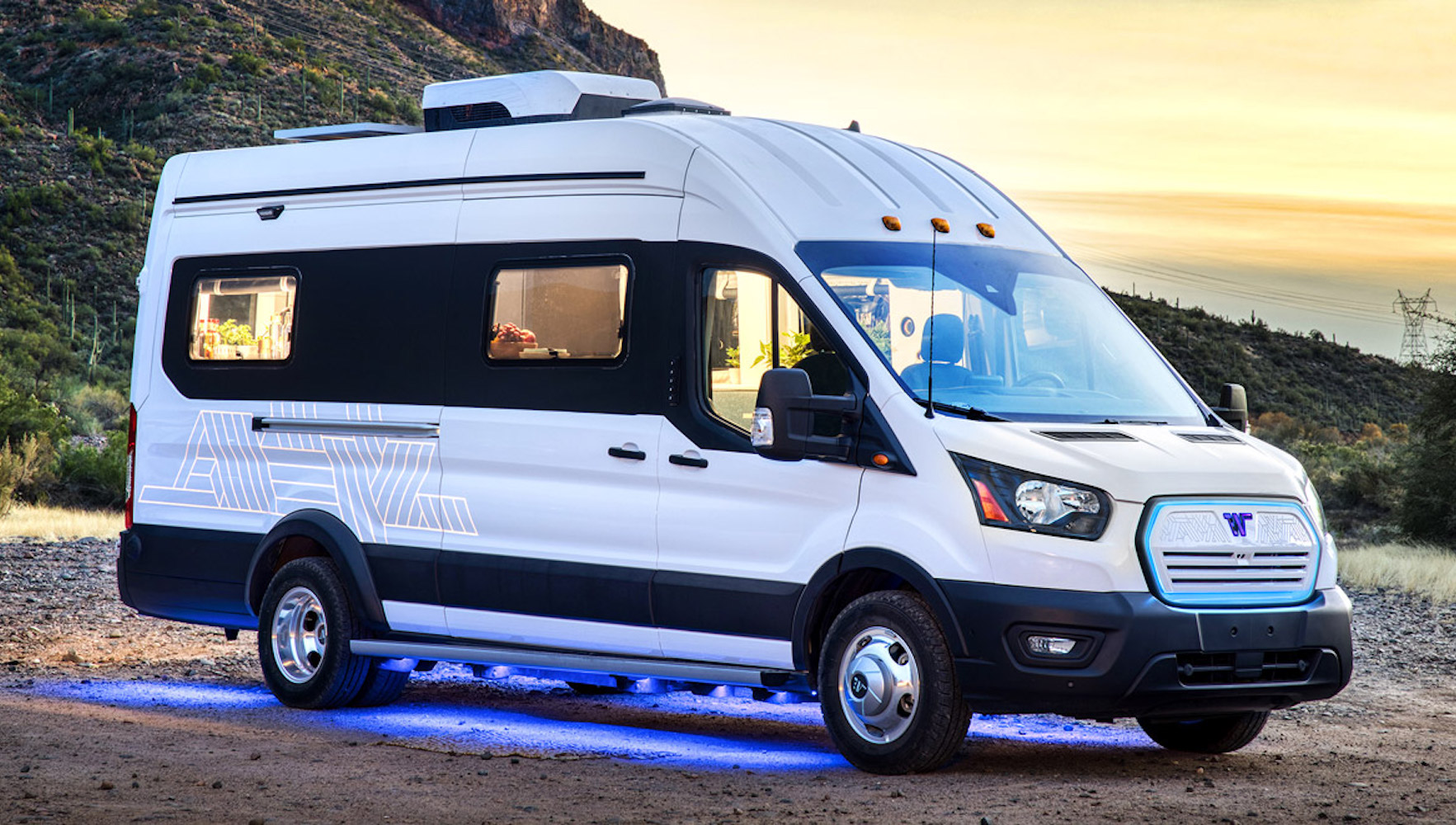 The Winnebago e-RV, an electric concept vehicle based on the Ford Transit van sitting on a road against a sunset in the background