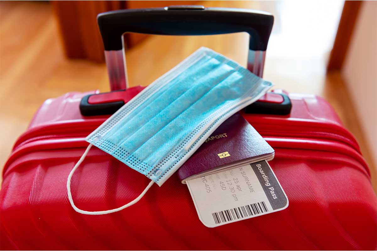a suitcase, mask and passport. According to Scott's Cheap Flights, you'll want to book your summer travel now, even with all the uncertainty regarding travel during Omicron