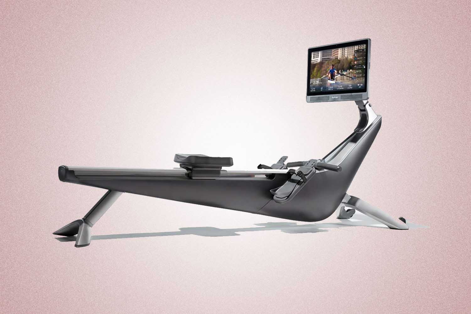 A grey rowing machine with a screen from Hydrow Rower, a perfect Valentine’s Day gift for 2022, on a pink background.