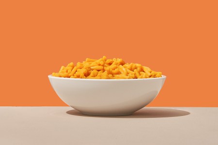 A bowl of mac and cheese on a table against an orange background. According to a new study, comfort food doesn't provide as much comfort as you may think.