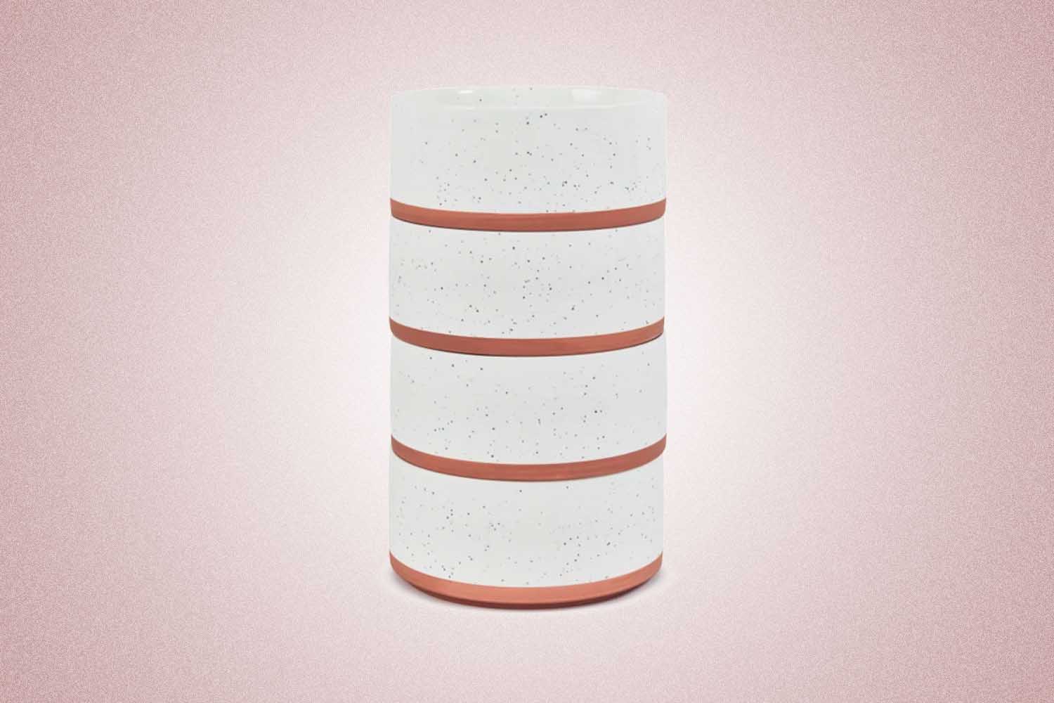 Four white speckled porcelain bowls with pink bottoms stacked on top of each other from Our Place, a perfect Valentine’s Day gift for 2022, on a pink background.