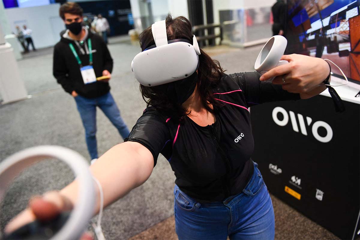 An attendee demonstrates the Owo vest, which allows users to feel physical sensations during metaverse experiences such as virtual reality games, including wind, gunfire or punching, at the Consumer Electronics Show (CES) on January 5, 2022 in Las Vegas, Nevada. - The CES tech show threw open its doors Wednesday in Las Vegas despite surging Covid-19 cases in the United States, as one of the world's largest trade fairs tried to get back to business. Despite some obvious gaps on the showfloor -- after high-profile companies like Amazon and Google cancelled over climbing virus risk -- crowds of badge-wearing tech entrepreneurs, reporters and aficionados poured through venues.