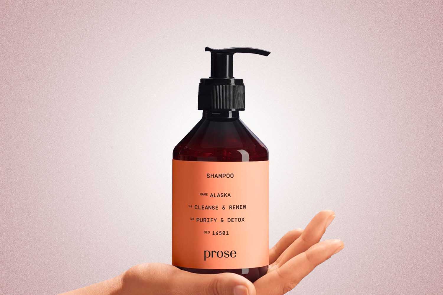 A hand holding a shampoo bottle from Prose, a perfect Valentine’s Day gift for 2022, on a pink background.