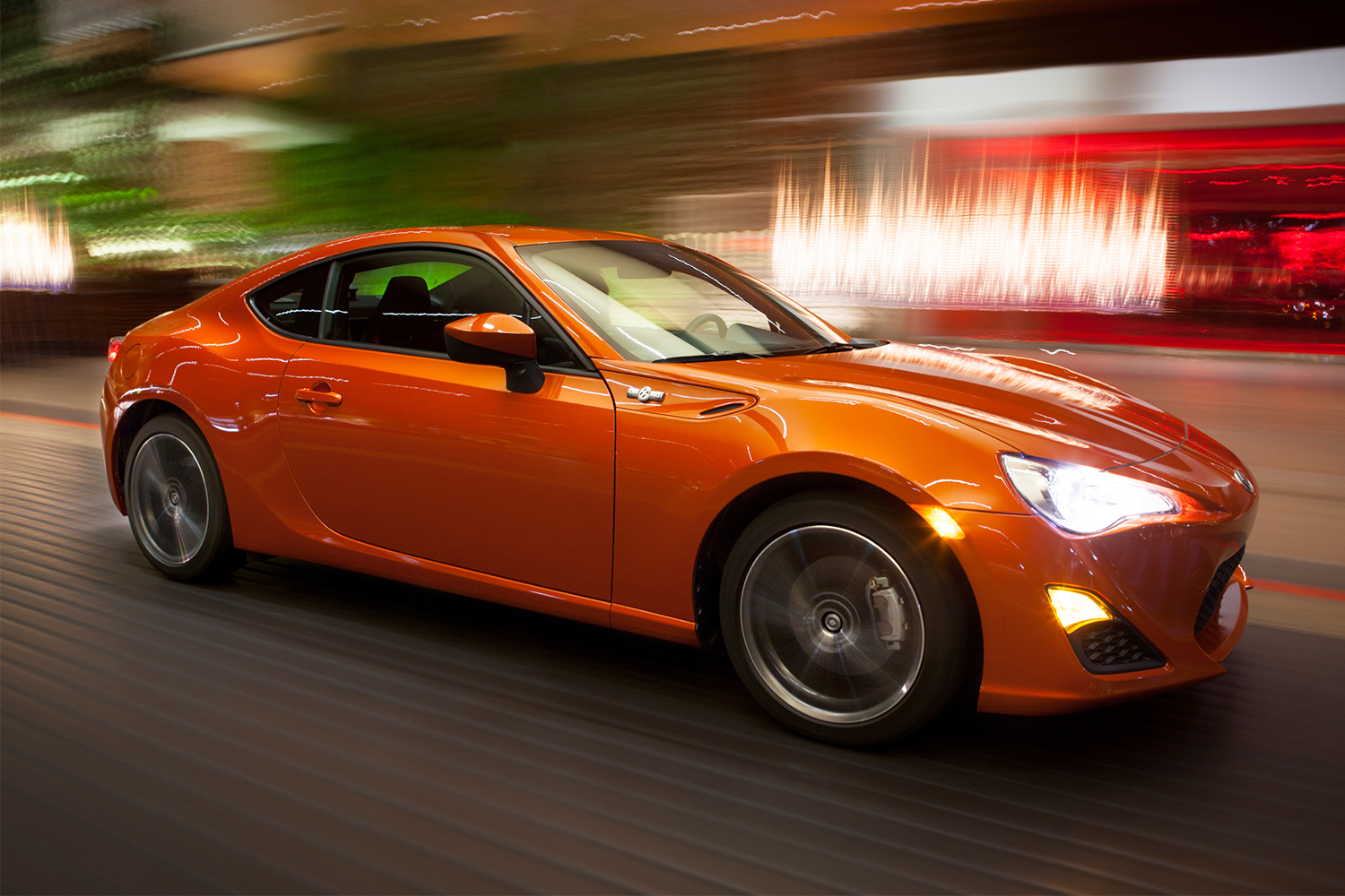 The 2013 Scion FR-S sports car in orange driving at night 