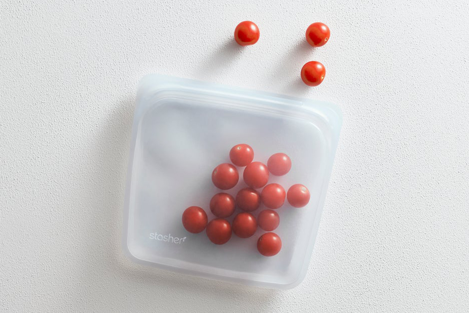 A clear Stasher storage bag with cherry tomatoes inside and laying on a table. Here's why you need these reusable platinum silicone bags in your kitchen and elsewhere.