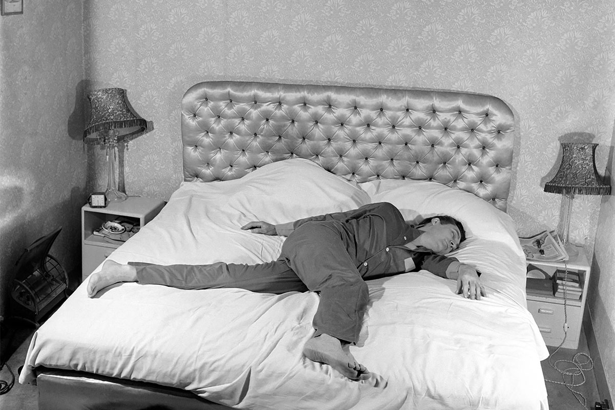 A man sprawled across a bed in black and white. Some sleepers prefer to wake up in the middle of the night, putter around for a couple hours, then head back to bed.