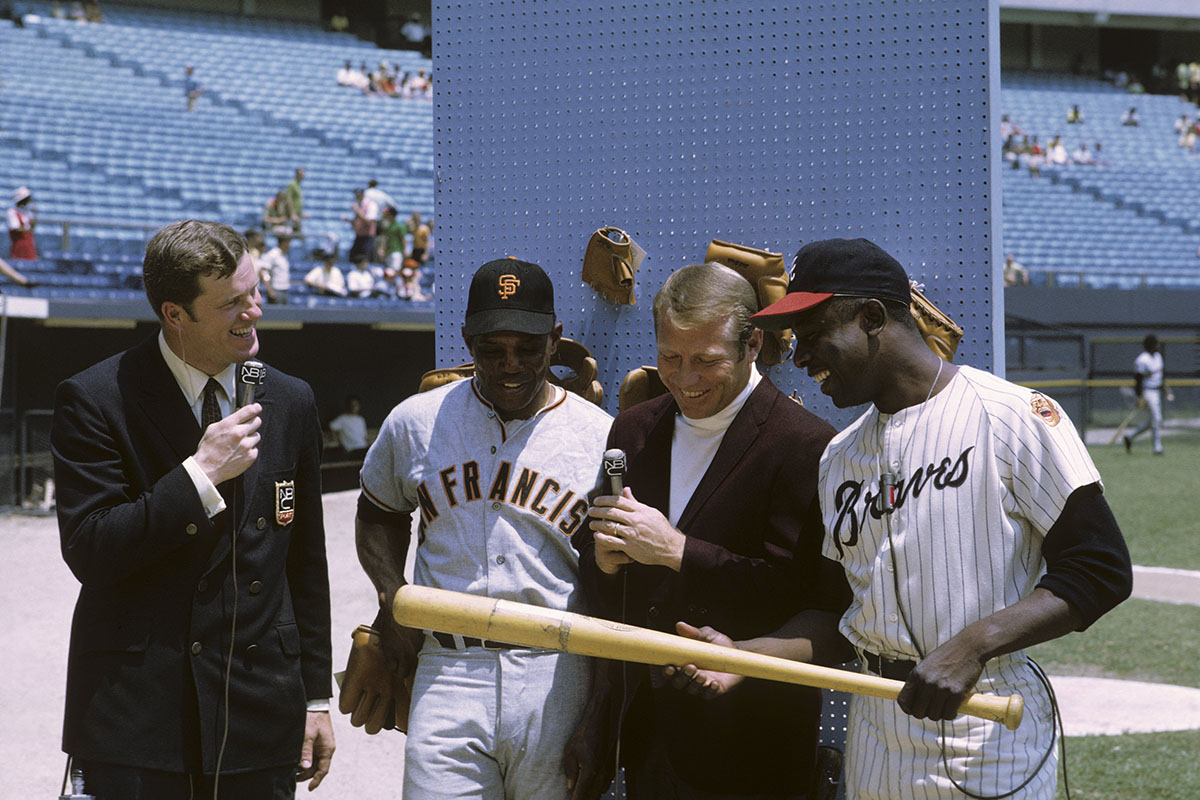 Mickey Mantle, Hank Aaron and Willie Mays inspect a baseball bat.
