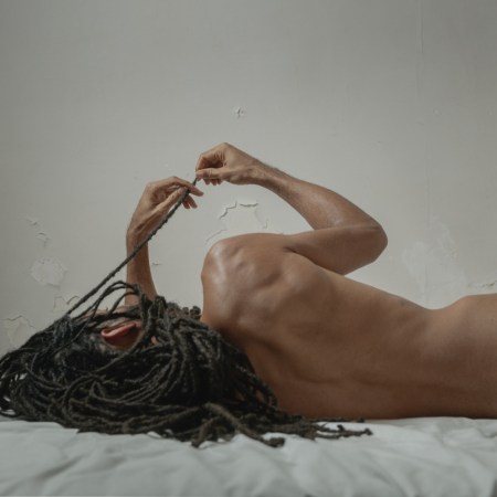 A nude man lies on a white bed with his back to the camera, posing for Laura Stevens' series of male nudes, "Him."