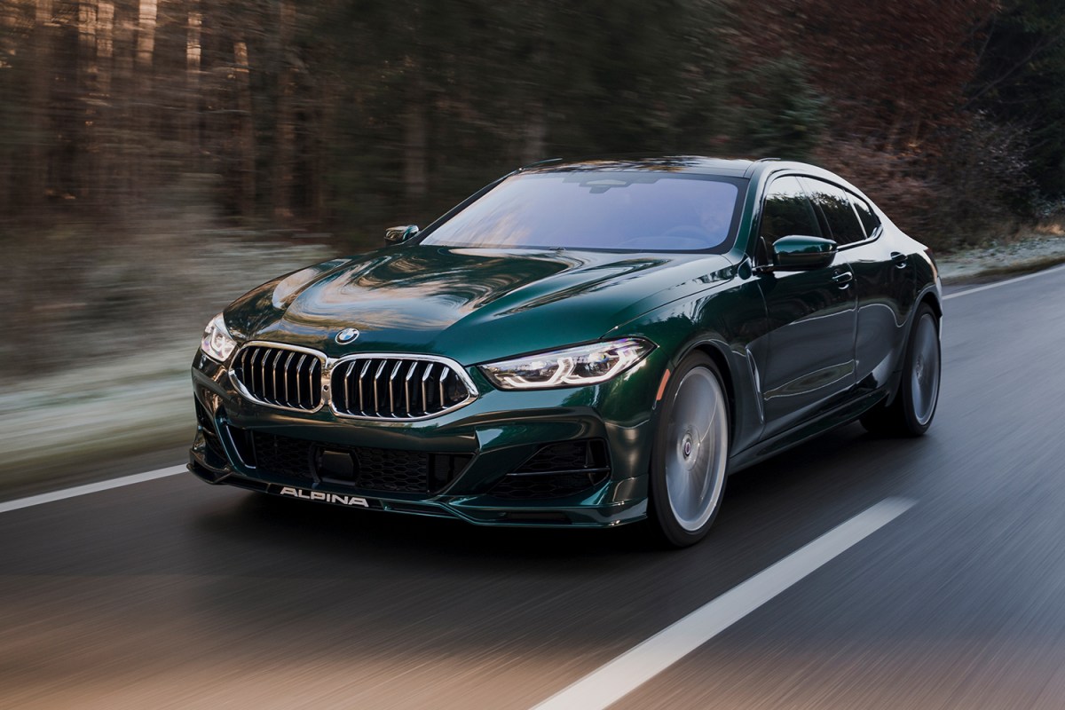 The 2022 BMW Alpina B8 Gran Coupe in the color Alpina Green Metallic driving down a road in the middle of the woods at sunset. We tested and reviewed the luxury car.