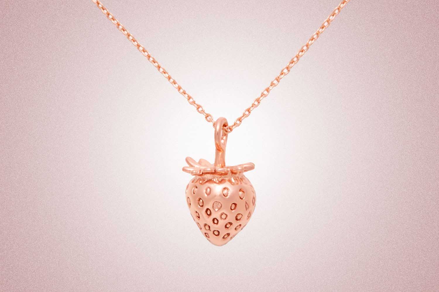 Rose gold necklace with a three-dimensional strawberry charm, a perfect valentine's day gift, on a pink background. 