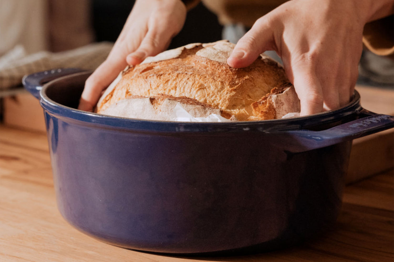 a loaf of bread being lowered into a dutch oven