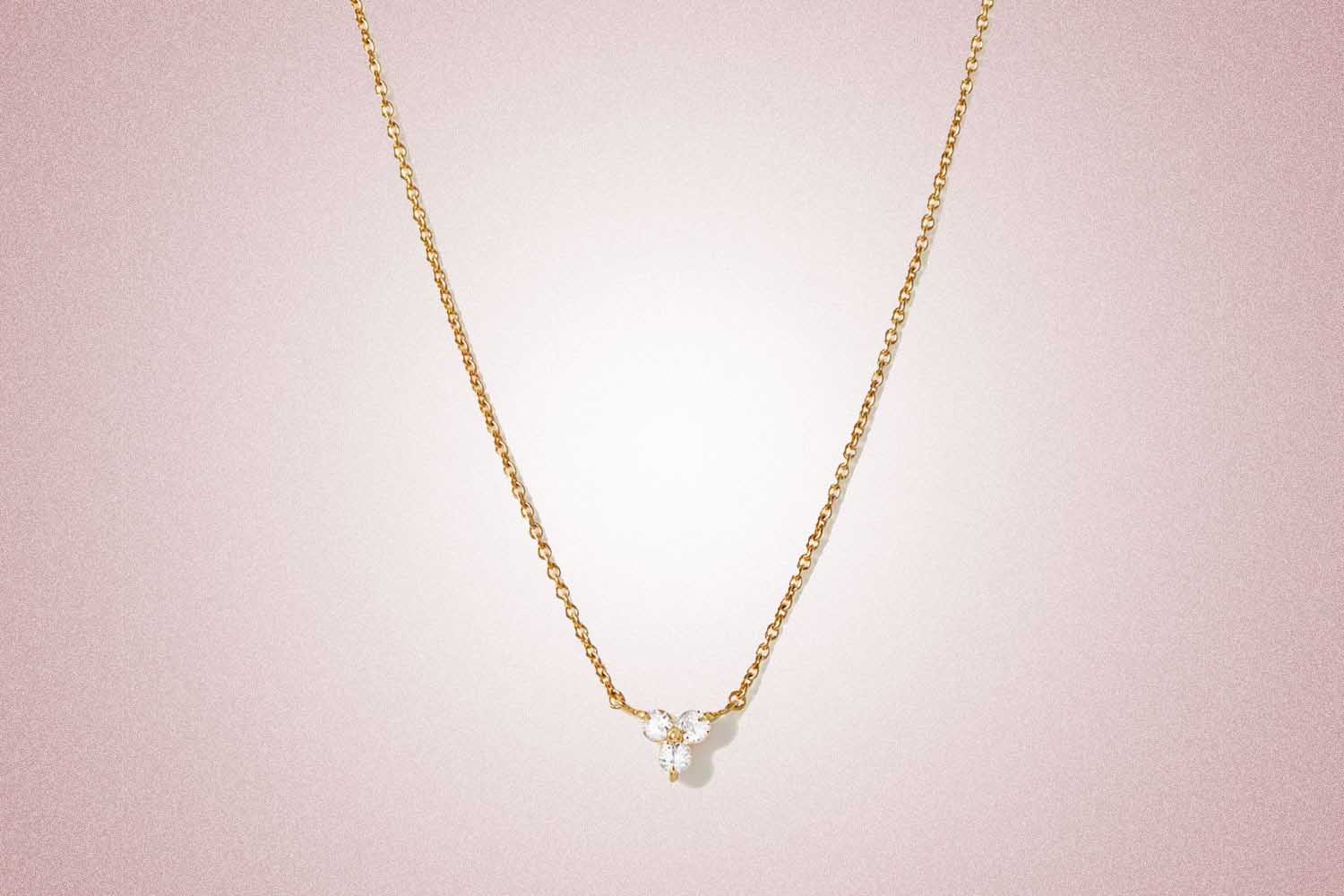A gold chain necklace with white sapphires in the shape of a lotus flower from Mejuri, a perfect valentine's day gift, on a pink background. 
