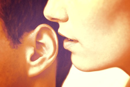 Close-up photo of a woman whispering into a man's ear