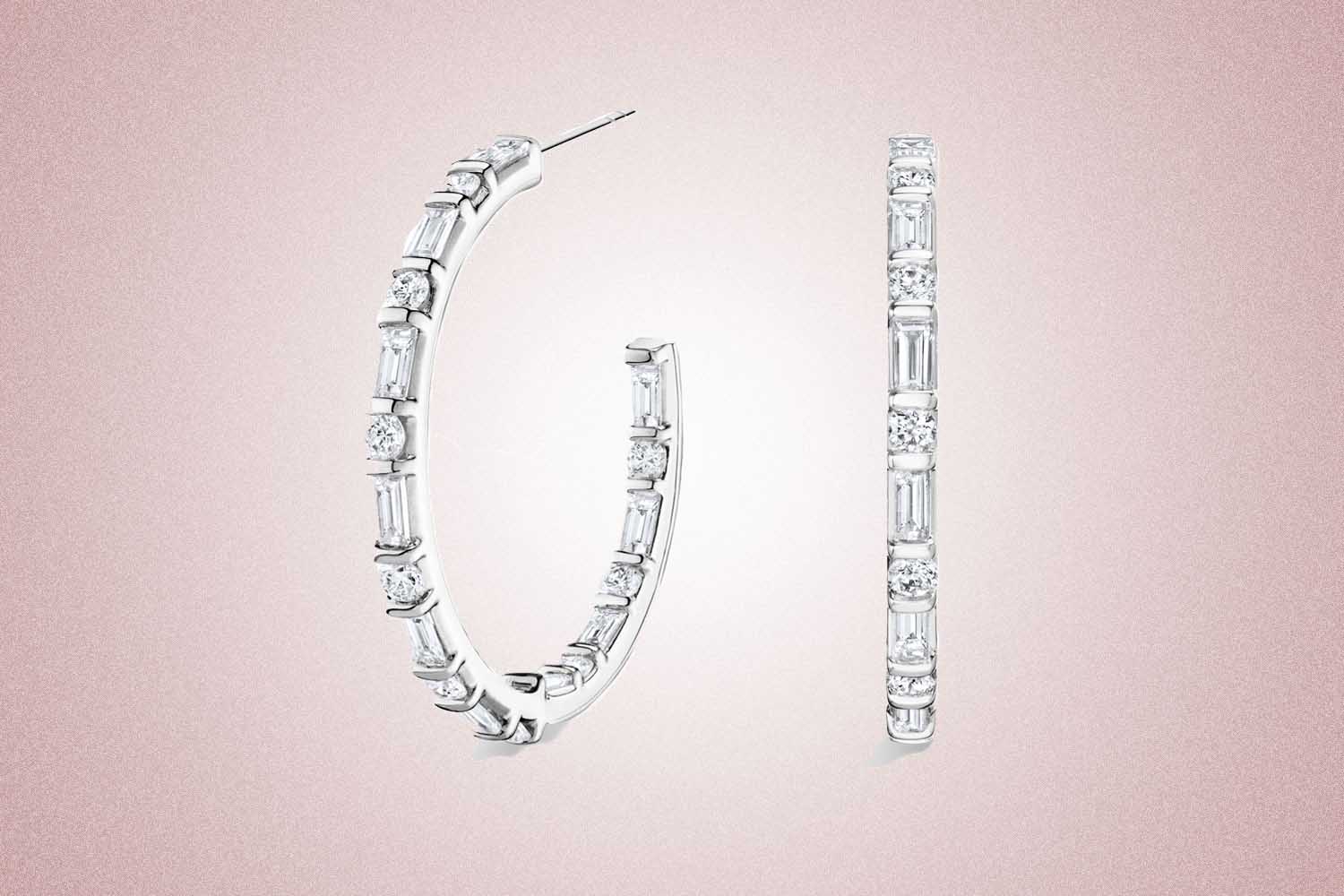 A pair of white gold diamond hoop earrings, a perfect valentine's day gift, on a pink background.