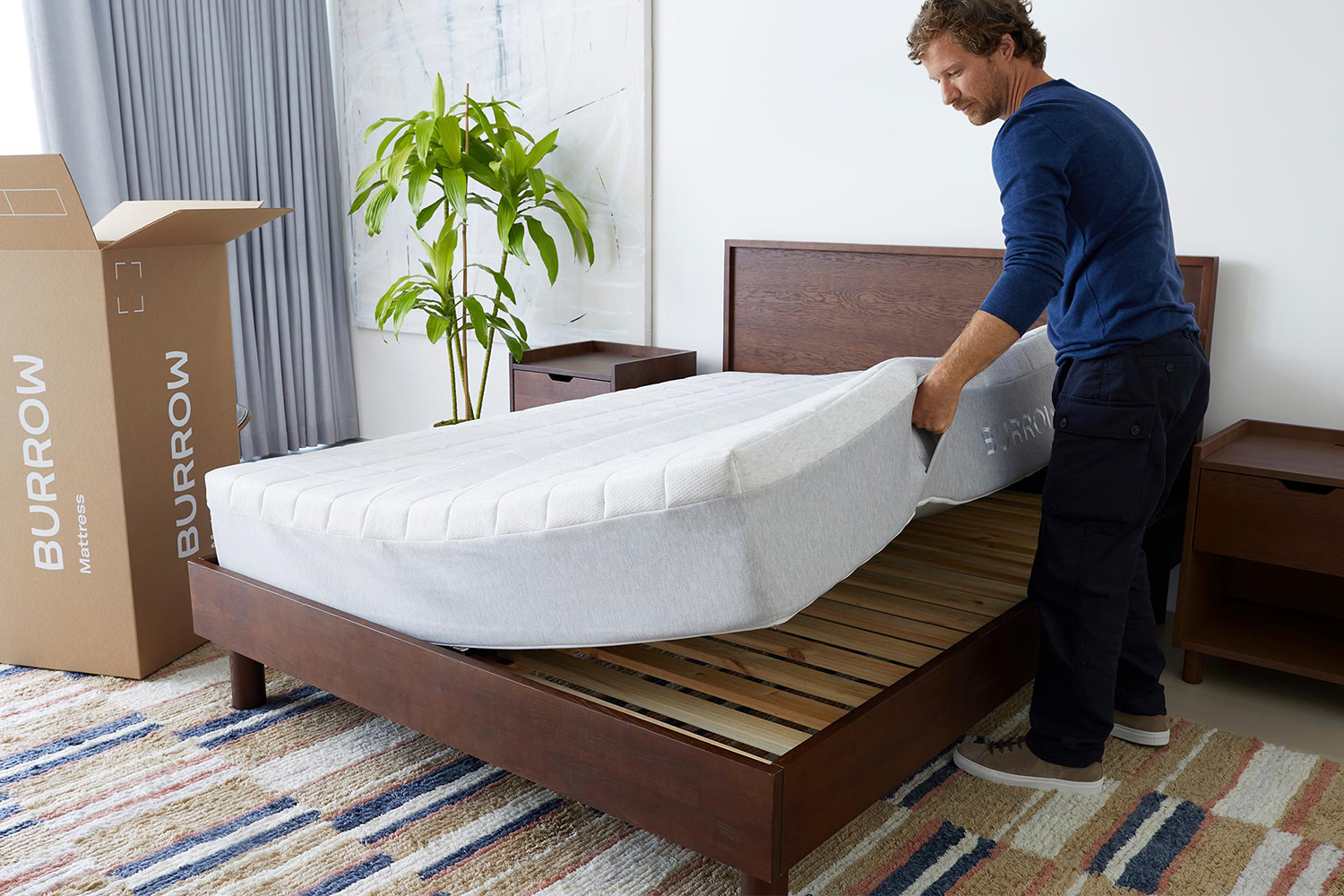 A man lowering a Lyric Mattress from Burrow onto the DTC furniture company's Circe Bed, both of which launched in February 2022