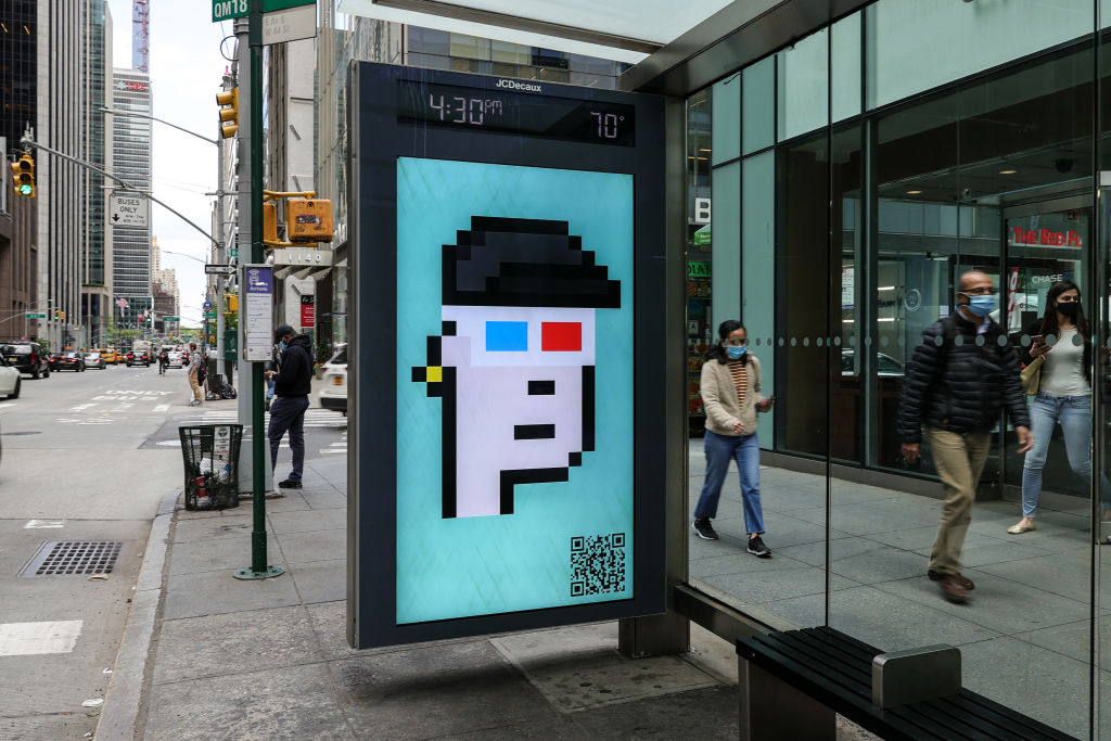 People wearing protective masks walk past a CryptoPunk digital art non-fungible token (NFT) displayed on an electronic billboard at a bus shelter in Midtown Manhattan. A recent CryptoPunks auction at Sotheby's was canceled at the last minute because the consignor withdrew the lot.