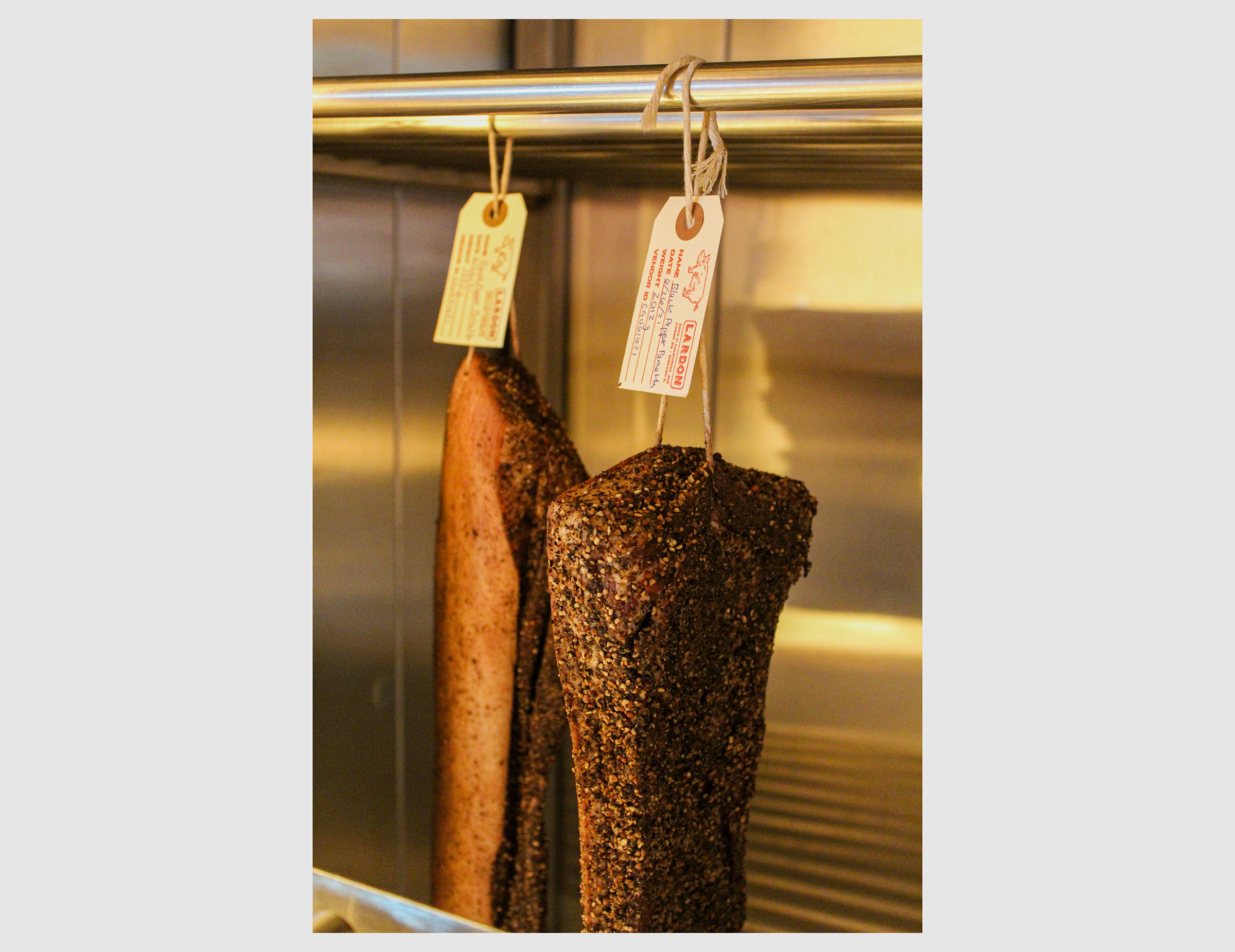 Two pieces of black pepper pancetta hang in the curing room at Lardon