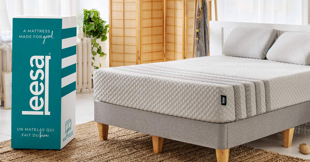 The Leesa Hybrid mattress sitting on a bed frame in a bedroom next to the box it came in. Leesa mattresses are up to $500 of for President's Day 2022.