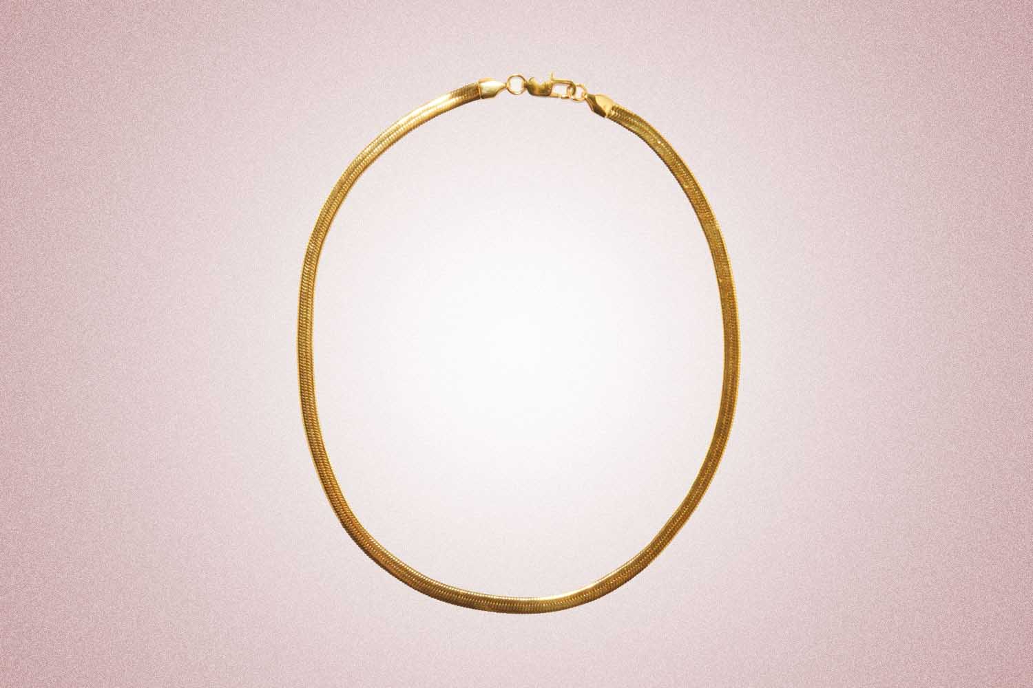 A simple gold-plated herringboe necklace, a perfect valentine's day gift, on a pink background. 