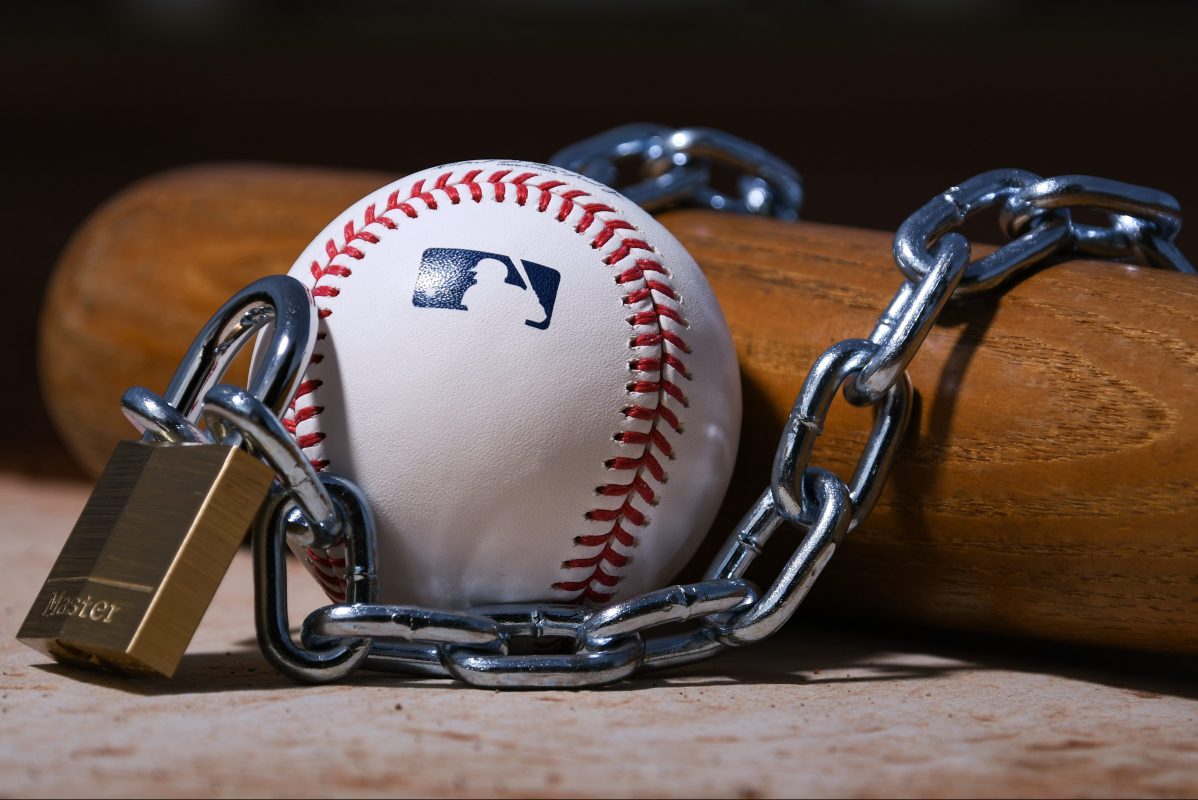 A Rawlings MLB baseball sits with a bat, lock and chain to represent the lockout