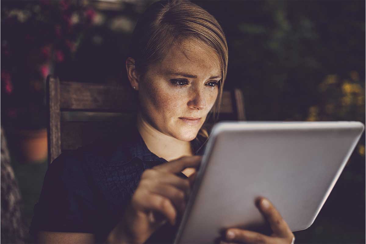 A blond woman staring at a tablet in a dark room. Online behavior was worse for women in 2021 over any other year, according to a new Microsoft study.