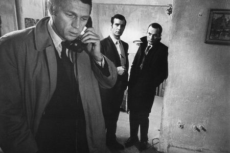 Bullitt (Steve McQueen) talks on the phone as 2 actors look on in a scene from the movie "Bullitt."