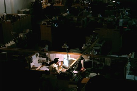 A man sitting at a lit cubicle in a dark office.