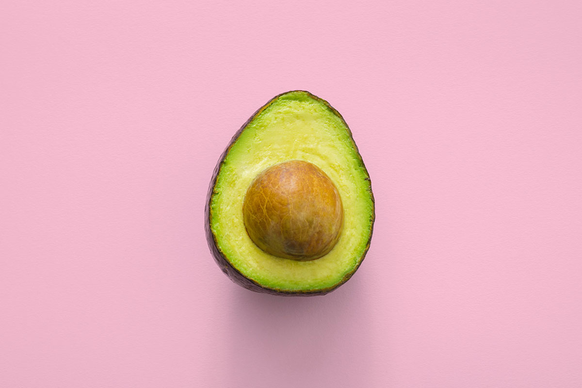 An avocado against a pink background.