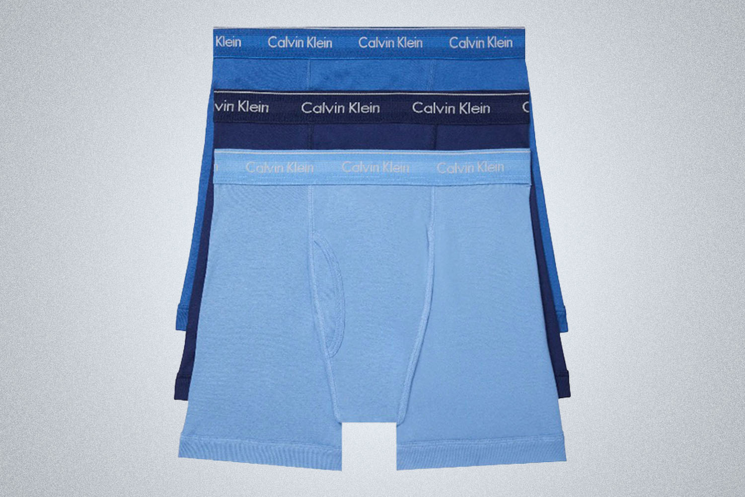 three overlayered Calvin Klien Boxer Briefs in 3 shades of blue with the logo waistband on a gray background