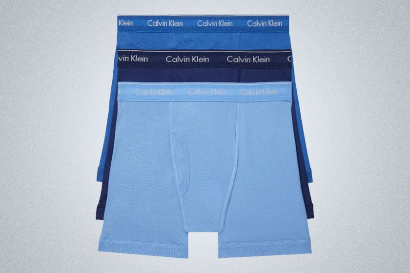 three overlayered Calvin Klien Boxer Briefs in 3 shades of blue with the logo waistband on a gray background