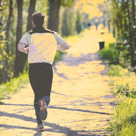 A man running along a wooded trail in springtime.